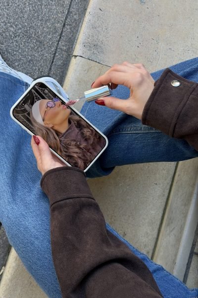 Mujer aplicándose lipstick mientras sostiene su teléfono con una foto de su rostro.