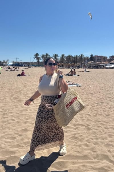 Handymar López paseando por la playa con look veraniego, bolso de rafia y gafas de sol, creando contenido UGC de lifestyle y viajes.