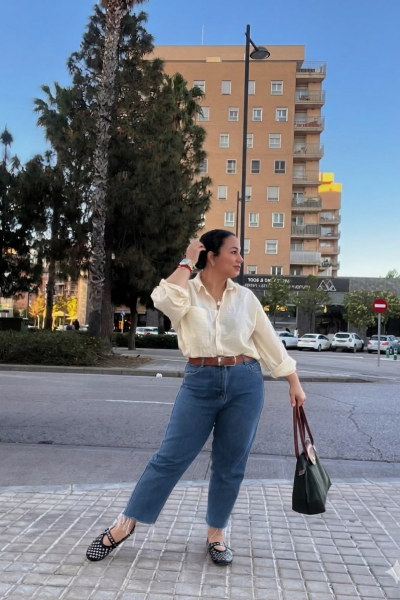 Handymar López posando en una calle urbana con camisa blanca, vaqueros y bolso de mano para contenido UGC de moda y lifestyle.