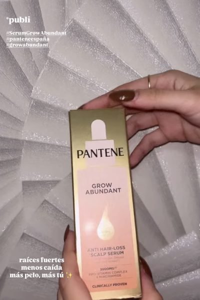 Serum Pantene Grow Abundant en caja dorada y rosa, sostenido por una mano con manicura, fondo gris texturizado.