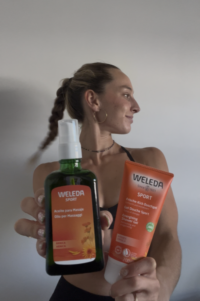 Creadora de contenido fitness mostrando productos Weleda Sport de árnica para masaje y ducha deportiva tras una rutina de ejercicio.