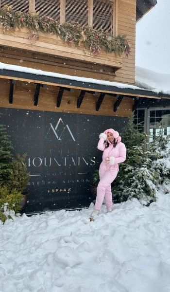 Isamar Florido Álvarez disfrutando del invierno en la nieve frente a un hotel en Sierra Nevada, luciendo un conjunto de abrigo rosa. Agencia de marketing digital Brilla Influencers y Comunicación.