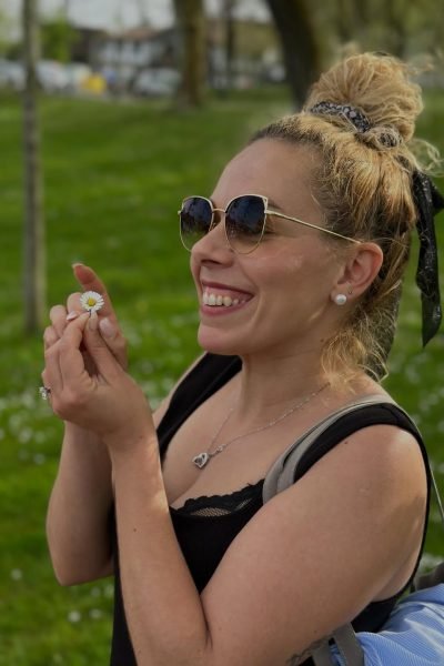 Jessica Circujano Gutiérrez sonriendo en un parque mientras sostiene una flor, mostrando un estilo de vida natural y cercano.