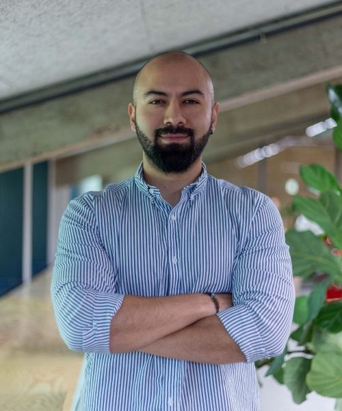 Juan Sebastián Cruz posando con los brazos cruzados, usando una camisa a rayas, con fondo de planta y ambiente moderno.