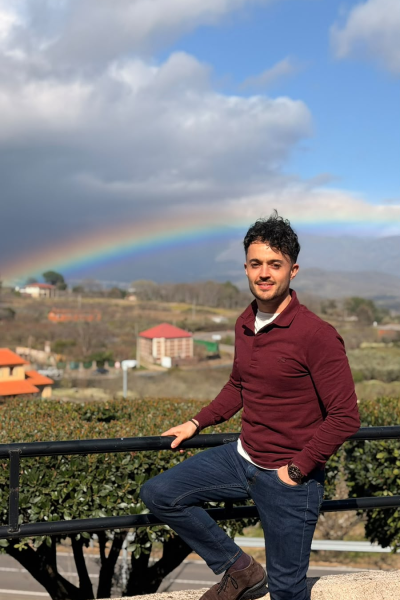 Julio Alcón García posando al aire libre frente a un paisaje natural con un arcoíris de fondo tras la lluvia.