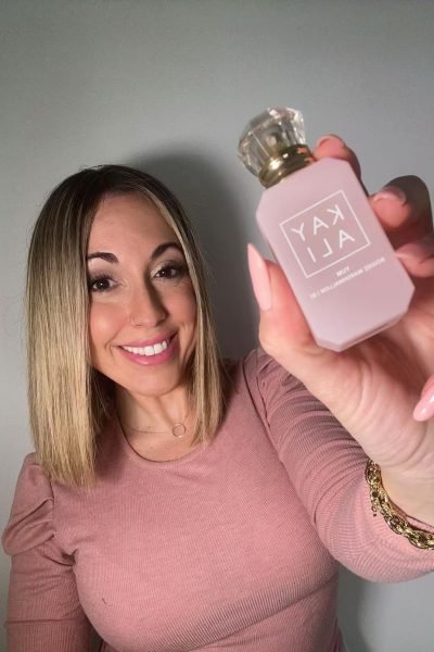 Laura Domínguez González mostrando una botella de perfume KAYALI, sonriendo a la cámara.