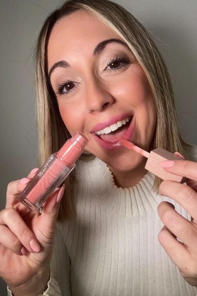 Laura Domínguez González aplicando gloss de labios, mostrando una sonrisa.