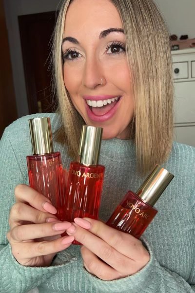 Laura Domínguez González sosteniendo tres frascos de perfume NOVOARGENT, sonriendo.