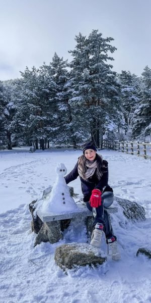 Laura Rojas posando en la nieve junto a un muñeco de nieve, en un paisaje montañoso. Agencia de marketing digital Brilla Influencers y Comunicación.
