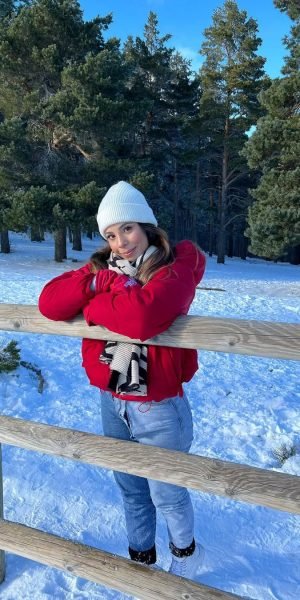Laura Rojas posando al aire libre en la nieve, con un abrigo rojo y bufanda, junto a una cerca de madera. Agencia de marketing digital Brilla Influencers y Comunicación.
