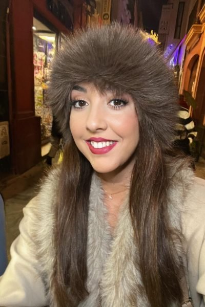 Lola Martín González usando un gorro de peluche en una noche iluminada con luces cálidas.