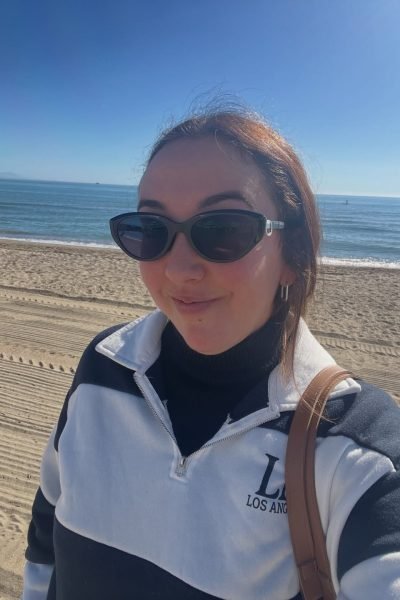 Lola Martín González en la playa con gafas de sol y camiseta de rayas en un día soleado.