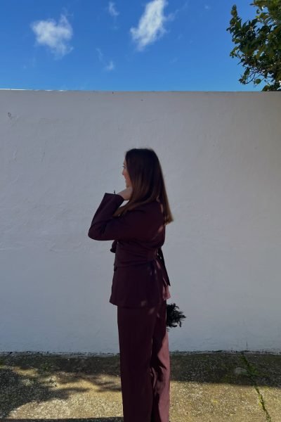 Lola Martín González posando con un conjunto de traje burdeos frente a una pared blanca.