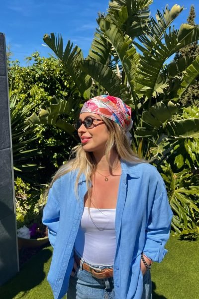 Lucía Cardona posando con un pañuelo de colores frente a plantas tropicales.