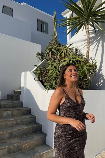 Lucía Pérez García posando al aire libre con vestido animal print en un entorno mediterráneo de arquitectura blanca y vegetación tropical.