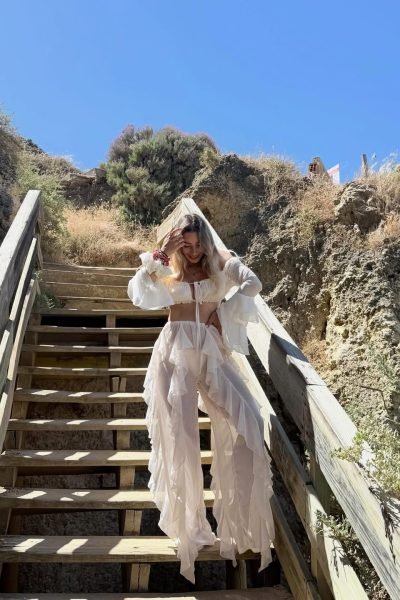 Mari López Jiménez posando en unas escaleras de acceso a la playa con un conjunto blanco vaporoso, creando contenido UGC de moda y lifestyle al aire libre.