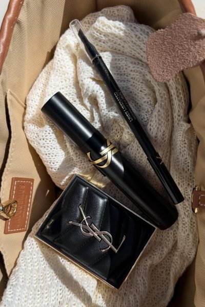Productos de maquillaje y belleza de lujo organizados en un bolso junto a prendas de punto, dentro de una sesión de contenido beauty creada por Mari López Jiménez.