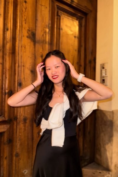 Agencia de marketing digital Brilla Influencers y Comunicación, María Bedins con vestido negro y suéter blanco, posando con las manos en el cabello frente a fondo de madera.