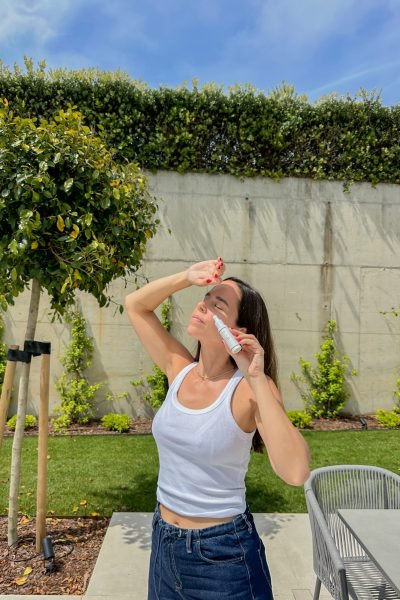 María Huidobro aplicando un producto cosmético en un jardín exterior durante una rutina de cuidado facial al aire libre.