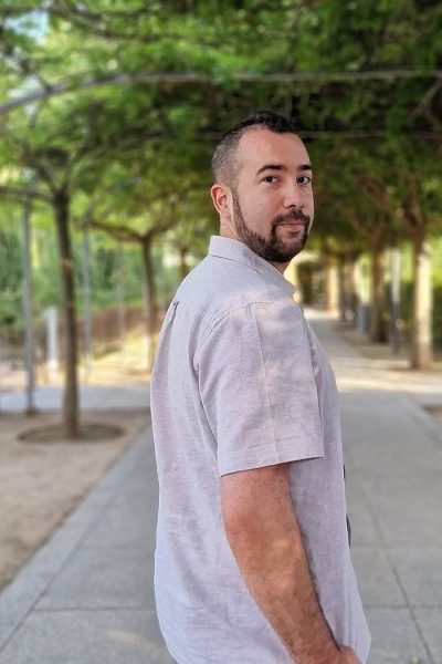 Miguel Tarjuelo mirando hacia atrás mientras camina por un camino rodeado de árboles. Title: Miguel Tarjuelo posando en un camino rodeado de árboles