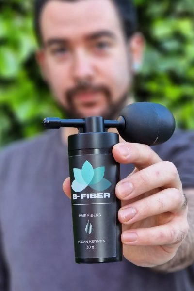 Miguel Tarjuelo sosteniendo un bote de B-Fiber para el cabello frente a un fondo verde.