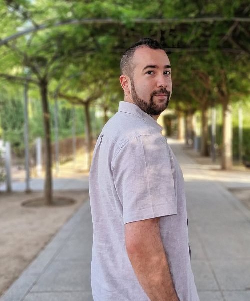 Retrato profesional de Miguel Tarjuelo, creador de contenido UGC, con barba y camiseta a rayas. Sonrisa amigable frente a fondo neutro.