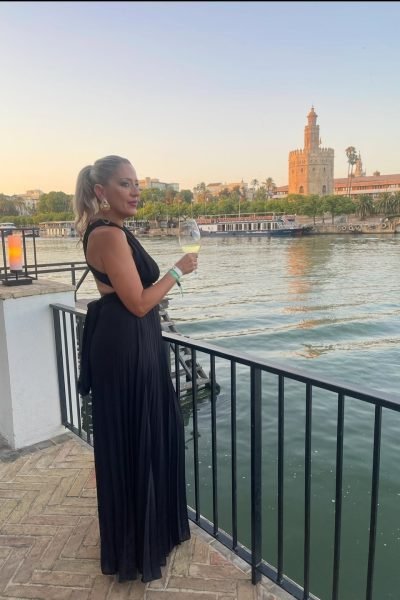 Noemí Bayona disfrutando de una copa de vino frente al río Guadalquivir con la Torre del Oro de Sevilla al fondo.