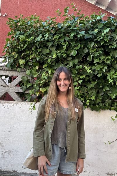 Patricia González posando al aire libre frente a una pared cubierta de hiedra, luciendo un outfit casual de estilo lifestyle con tonos naturales.