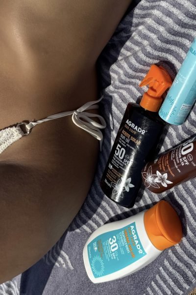 Un entorno natural con Paula Alsina mostrando una postura relajada, rodeada de productos de cuidado solar y con una actitud despreocupada.