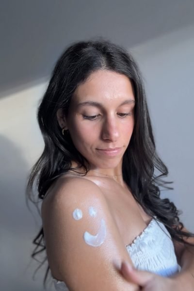 Primer plano de Paula Alsina con el sol resaltando su rostro, mostrando una sonrisa cálida mientras usa productos cosméticos.