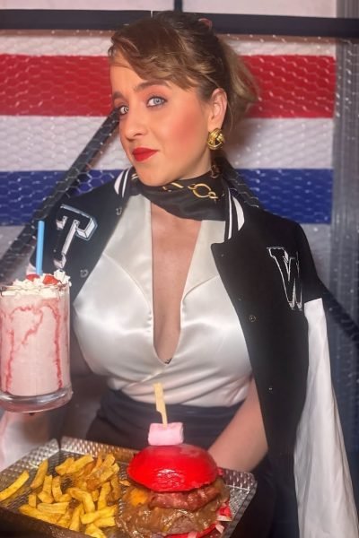 Rosa Alcázar Morales de Valencia posando con hamburguesa con pan rojo y batido rosa, mostrando estilo moderno y foodie