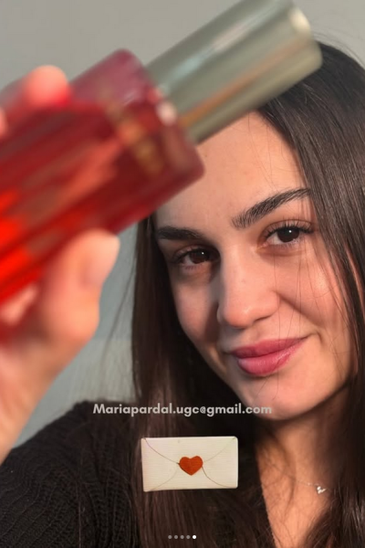 María mostrando un frasco rojo de producto de belleza, primer plano de su rostro sonriente.