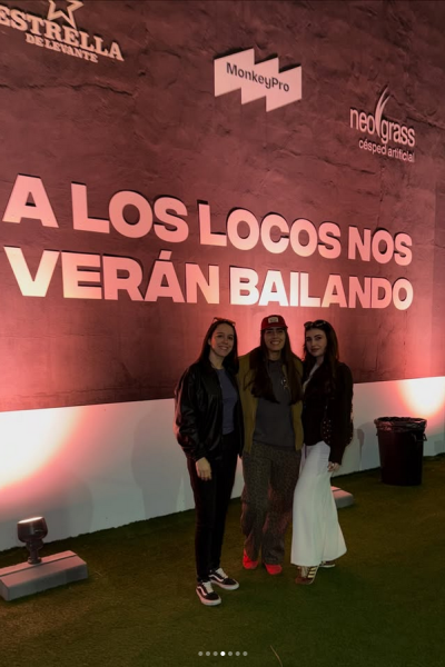 Tres mujeres posando juntas en un evento frente a un fondo con la frase “A los locos nos verán bailando”.