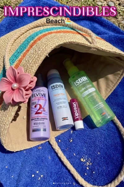Bolsa de playa con productos de cuidado personal y protección solar, sobre toalla azul.
