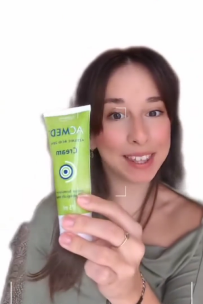 Mujer mostrando una crema facial con sonrisa natural, enfocando el producto en primer plano.