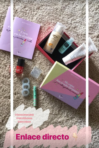 Flat lay de Birchbox abierta mostrando varios productos de belleza como esmaltes, cremas y accesorios, sobre fondo de alfombra clara.