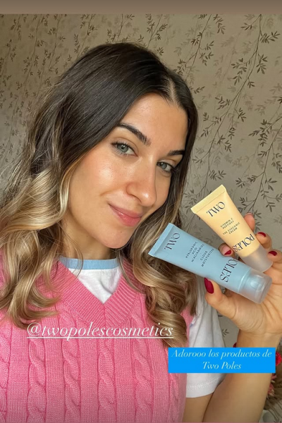 Joven sonriendo mientras muestra dos productos de cuidado facial de la marca Two Poles Cosmetics.
