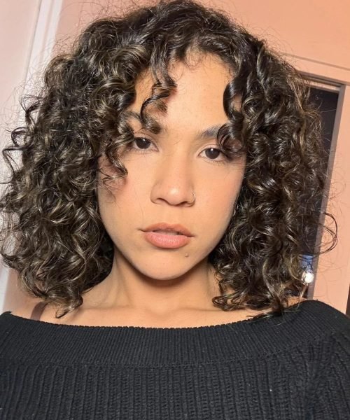 Agencia de marketing digital Brilla Influencers y Comunicación, mujer con rizos, top negro, frente a fondo claro.