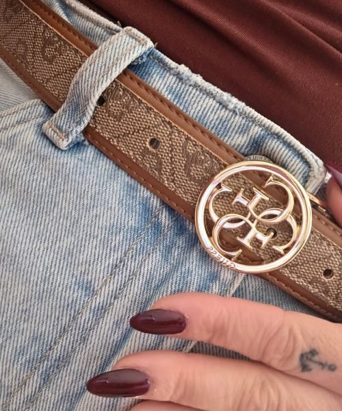 Detalle del cinturón de marca con hebilla dorada, jeans claros y uñas en color burdeos.