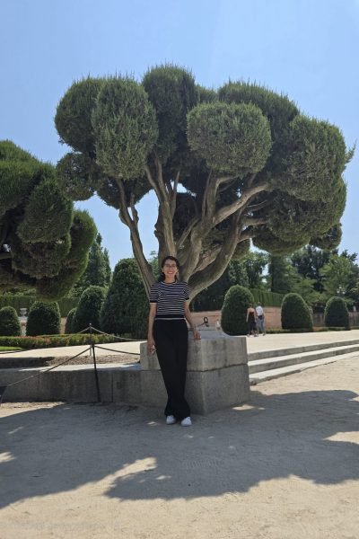 María del Carmen Ramírez, creadora UGC, posando junto a un árbol en un parque, disfrutando de un día soleado.