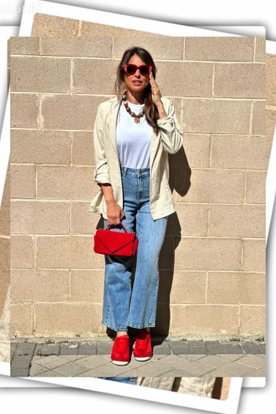 Mujer con gafas rojas, bolso rojo y zapatos deportivos rojos, posando frente a una pared de ladrillo.