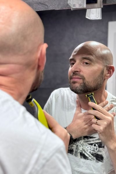 Hombre afeitándose la barba frente al espejo con una maquinilla de afeitar.