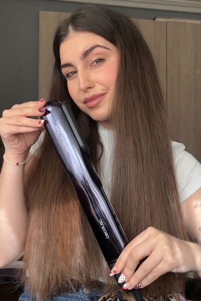 Mujer joven mostrando una plancha de pelo mientras sonríe, con cabello largo y liso.