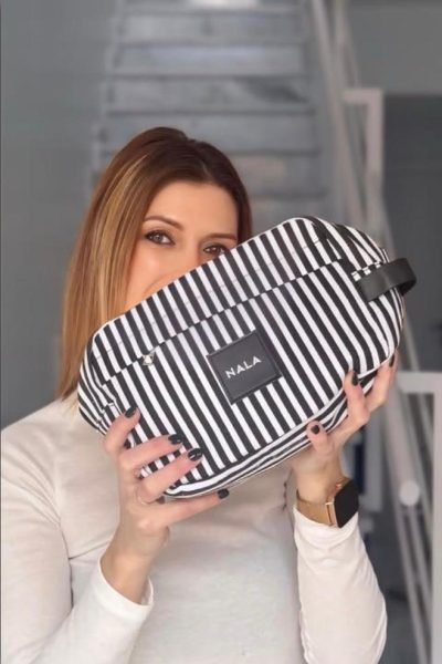 Mujer joven mostrando un bolso de rayas blancas y negras de la marca NALA frente a su rostro.