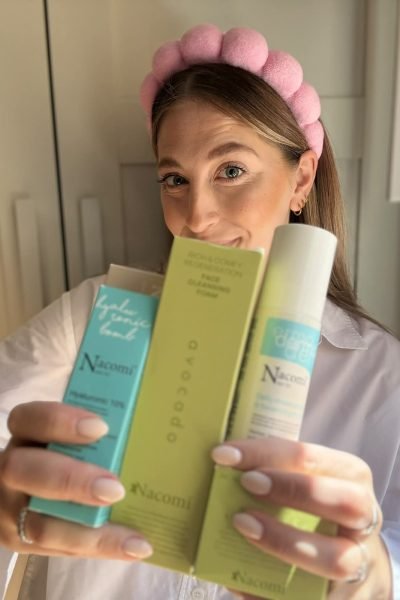 Mujer sosteniendo productos de cuidado facial de la marca Nacomi, usando una diadema rosa.