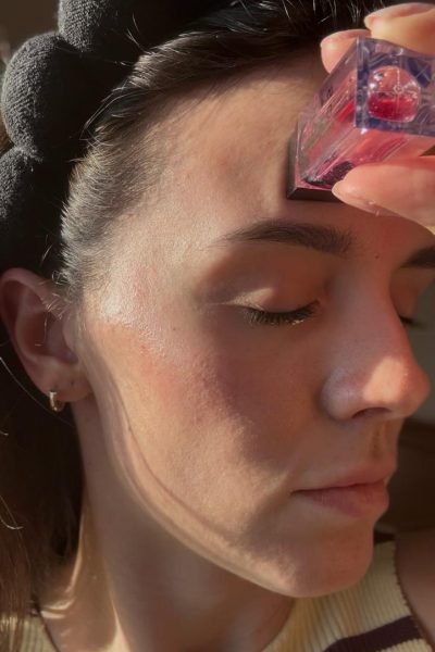 Primer plano del rostro de Esther Arribas Checa con los ojos cerrados aplicándose un dispositivo de masaje o producto cosmético transparente y rosa en la frente.