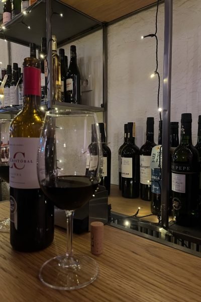 Copa de vino tinto y botellas en la barra del bar, con luces tenues en el fondo, capturada por Cristina Jiménez UGC.