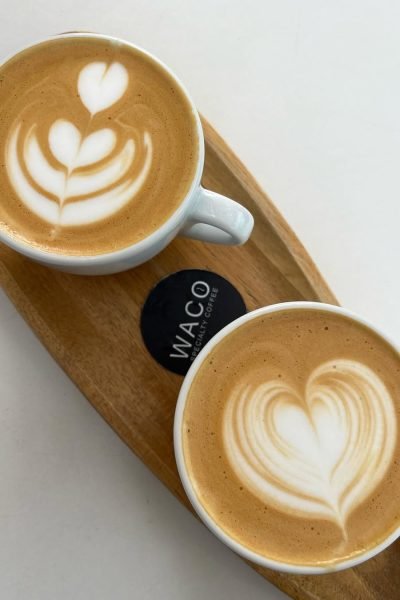 Café con arte latte servido en dos tazas sobre una bandeja de madera de Waco Specialty Coffee, capturado por Cristina Jiménez UGC.