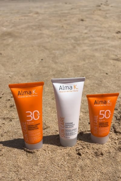 Alexandra Suciu mostrando productos de Alma K. para el cuidado solar mientras disfruta de un día en la playa.