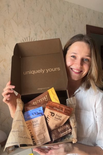 Alexandra Suciu mostrando una caja de productos Ohmy, sonriendo mientras presenta el contenido de la caja de snacks.